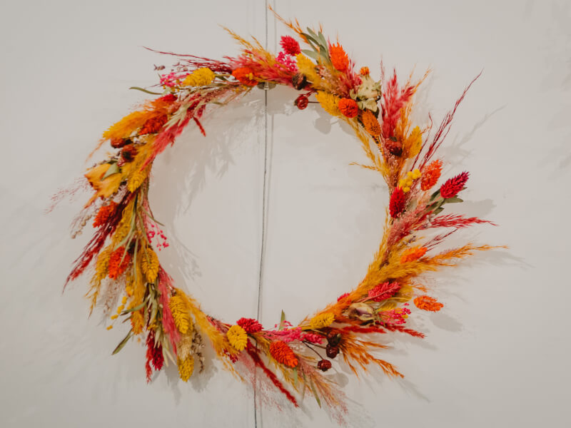 A red and orange DIY Christmas wreath on a white wall.